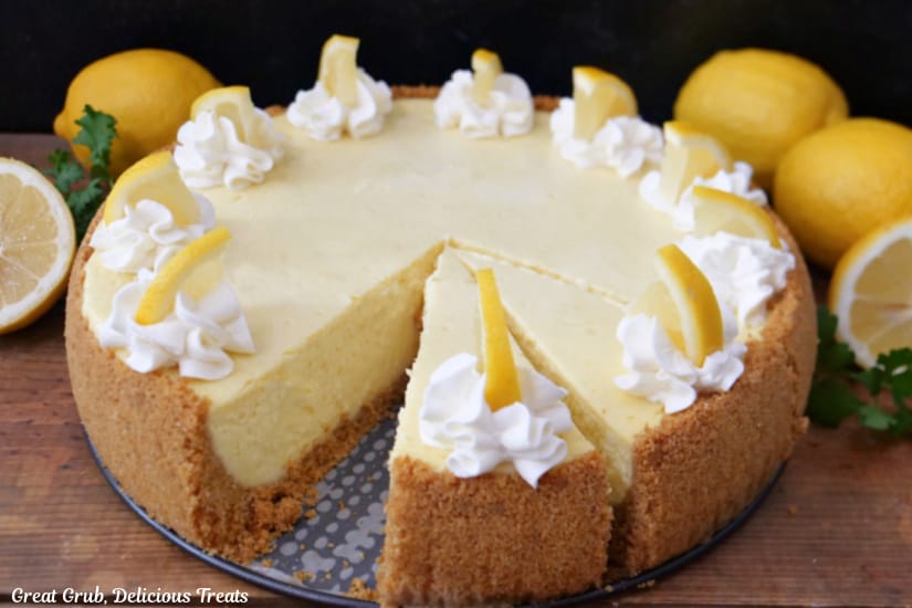 A horizontal photo of a whole lemon cheesecake with a slice removed.