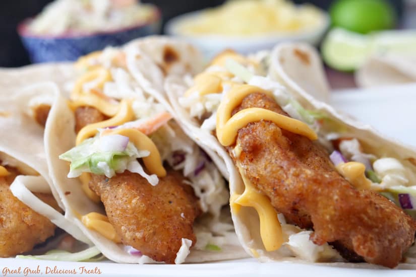 Three fish tacos in flour tortillas on a white surface.