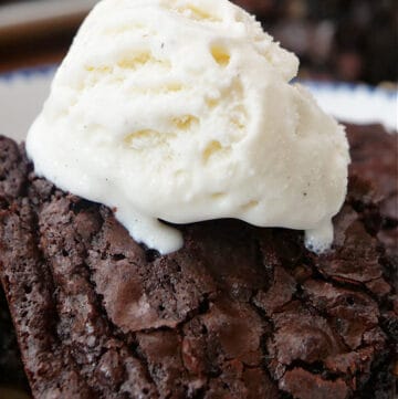 A close up photo of a chocolate brownie with a scoop of vanilla ice cream on top.