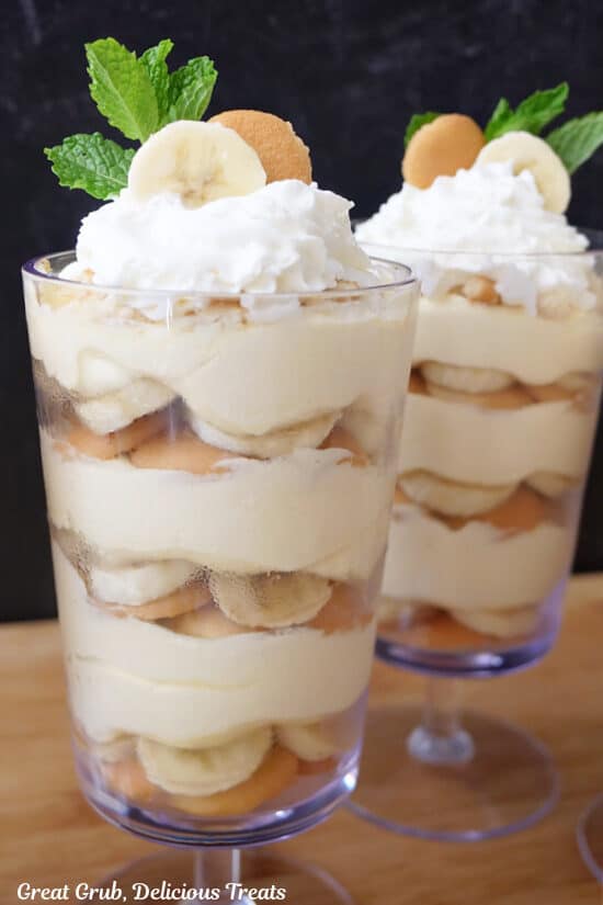 A close up of two banana pudding parfaits on a wood surface.