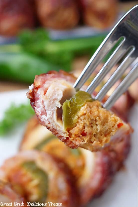 A close up of a fork with a bite of bacon wrapped chicken, jalapeño and sausage cream cheese filling.
