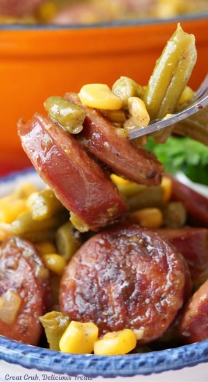 A close up of a bite of sausage, green beans and corn on a fork.