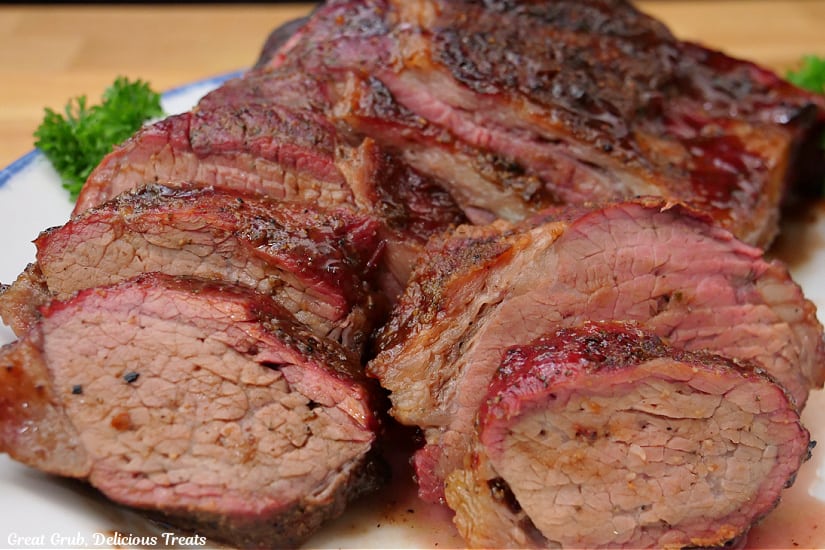 A horizontal photo of a smoked tri tip on a white plate with some of it sliced.