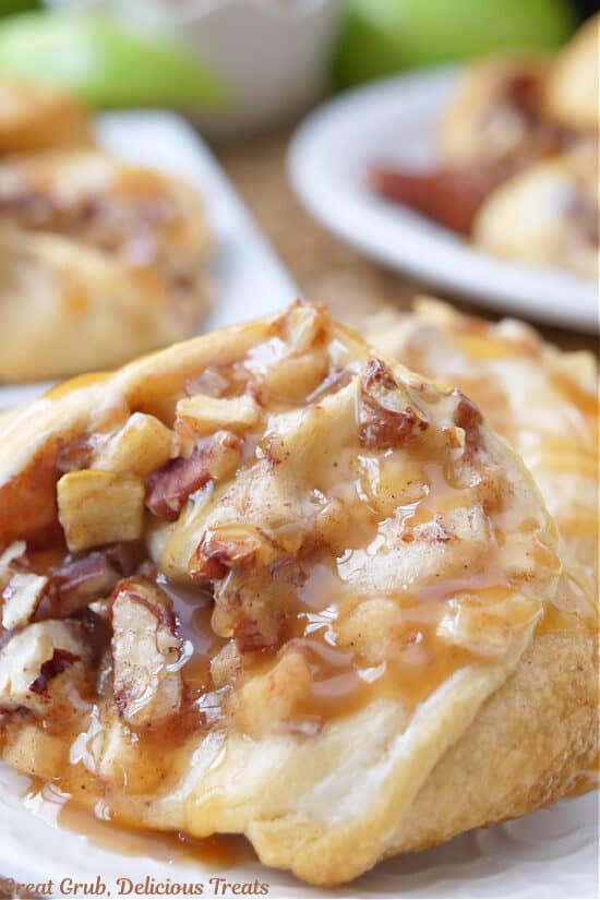A close up photo of an apple crescent roll with chopped apples, cream cheese and chopped pecans, and drizzled with caramel.