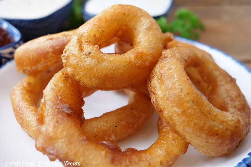 A horizontal photo of five onion rings on a white plate with blue trim.