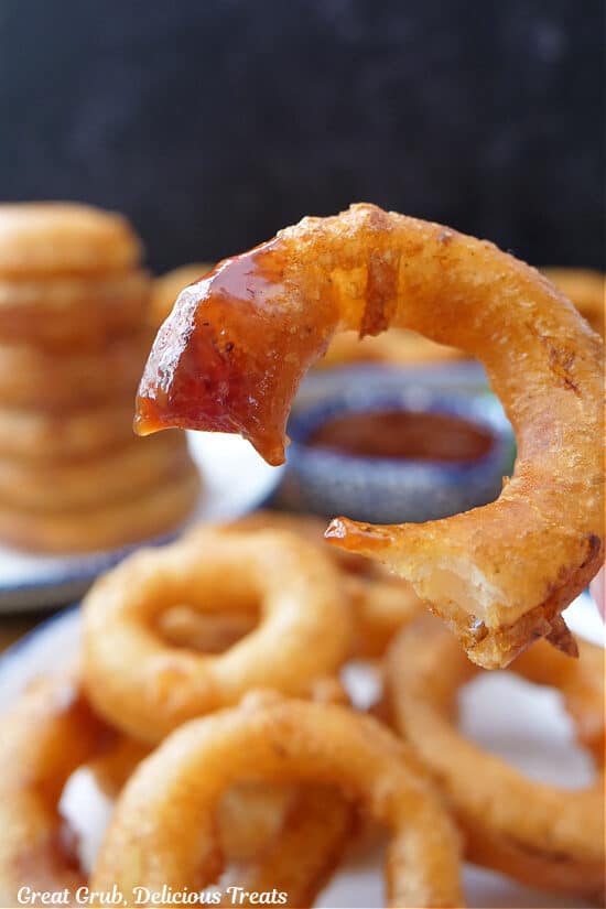 A close up of an onion ring that was dipped in barbecue sauce and a bite taken out of it.