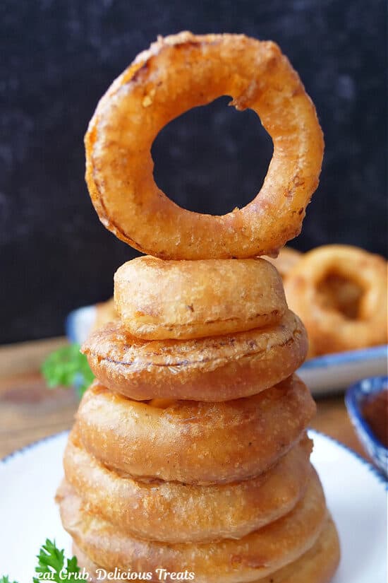 A stack of seven onion rings on a white plate with the top onion ring standing upright.