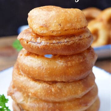 A stack of six onion rings on a white plate.
