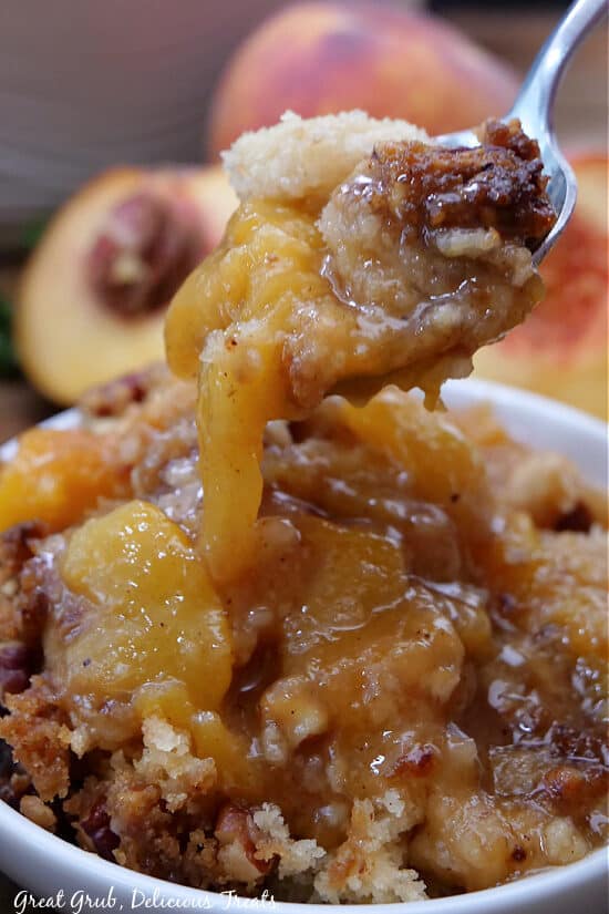 A close up photo of a spoonful of peach cobbler on it.