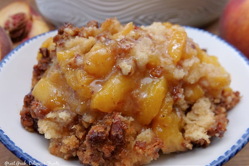 A horizonal photo of a shallow white bowl filled with the best peach cobbler recipe.