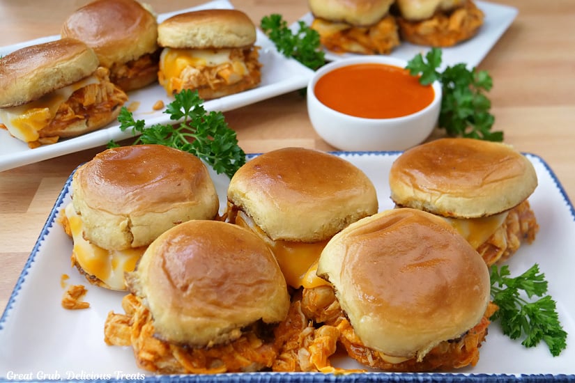 A horizontal photo of three white plates with buffalo chicken sliders on them with a small white bowl of buffalo sauce in the middle.