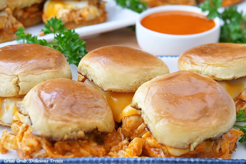 A horizontal photo of a white plate with blue trim with five chicken sliders on it.