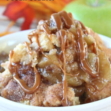 A white bowl filled with a serving of apple cobbler with pecans and caramel.
