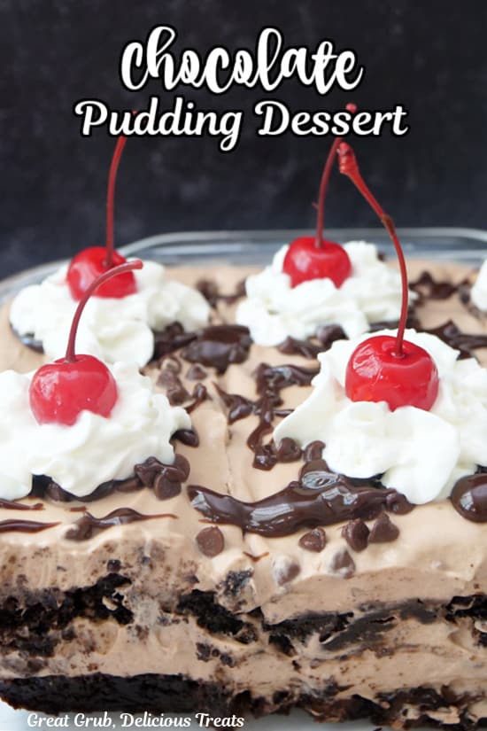 A chocolate layered dessert with brownies and chocolate pudding with whipped cream and cherries on top.