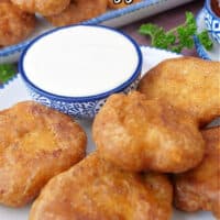 A white plate with blue trim with homemade chicken nuggets on it and a small blue bowl filled with ranch dressing.