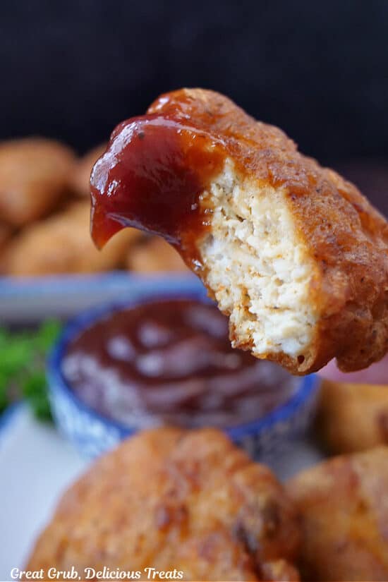A close up of a chicken nugget that has a bite taken out of it that has barbecue sauce on it.