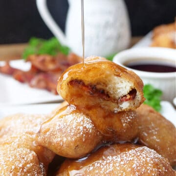 A stack of pancake bites with bacon in them on a white plate with syrup being drizzled over the top.