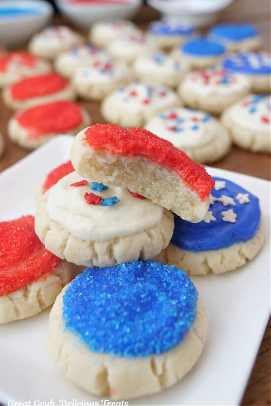 Red, with and blue bite-size sugar cookies on a white plate with a bite taken out of one of the cookies.