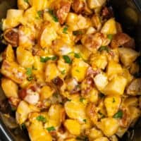 A crock pot filled with diced potatoes, bacon, cheese, onions, and more,