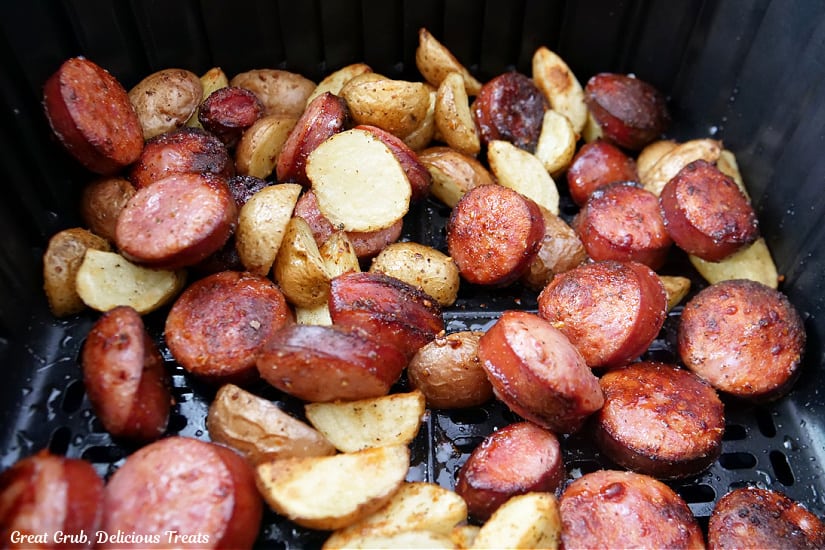 The air fryer basket with cooked smoked sausage and potatoes in it after it is finished cooking.