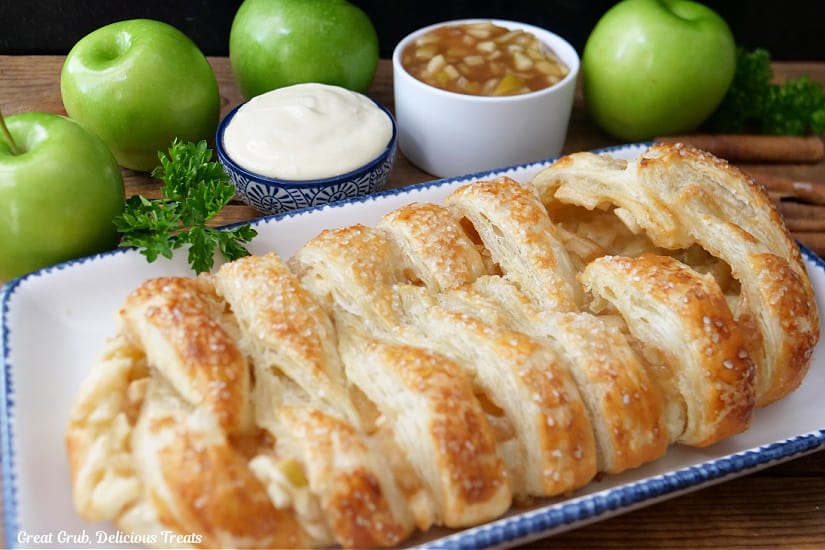 A horizontal photo of a white plate with blue trim with an apple puff pastry braid on it before being sliced into servings.