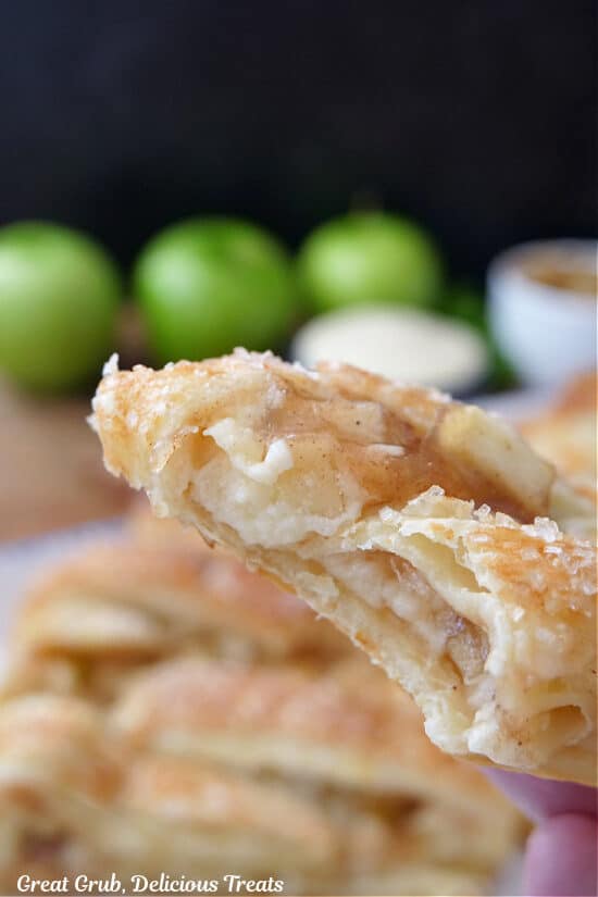 A slice of apple pastry braid with a bite taken out of it held up close to the camera lens.