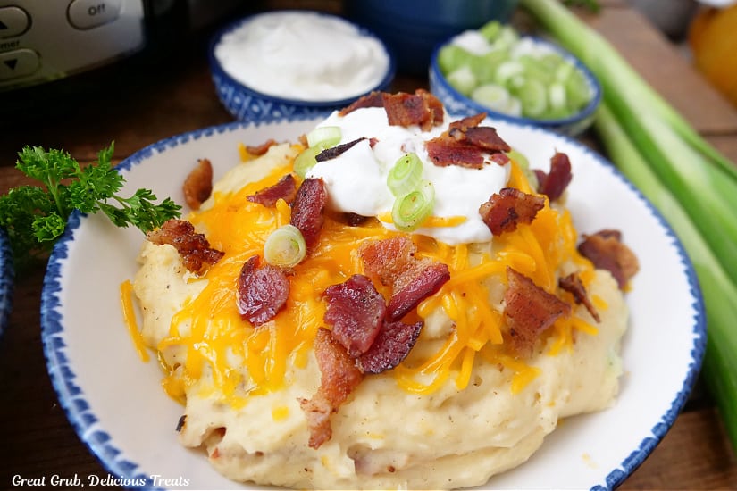 A horizontal photo of a serving of loaded mashed potatoes in a white bowl with blue trim.