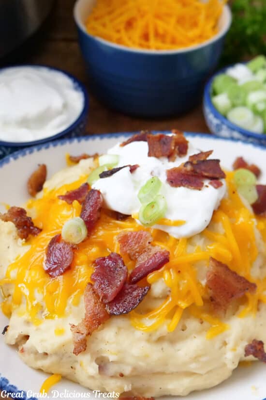 A bowl of creamy crock pot potatoes with cheese, bacon, green onions and sour cream on them.