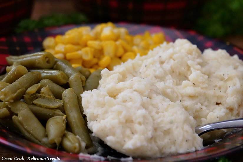 A horizontal photo of a plate filled with mashed potatoes, corn and green beans.