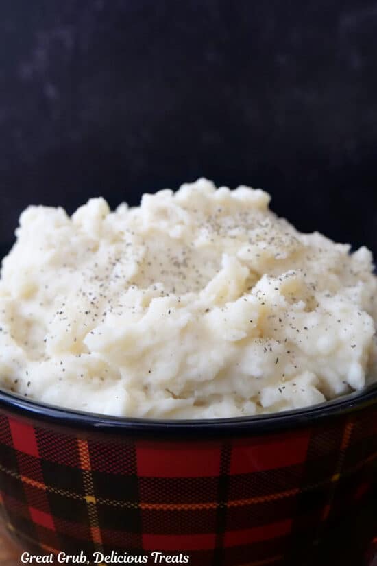 A red and black plaid bowl filled with a heaping serving of fluffy mashed potatoes.