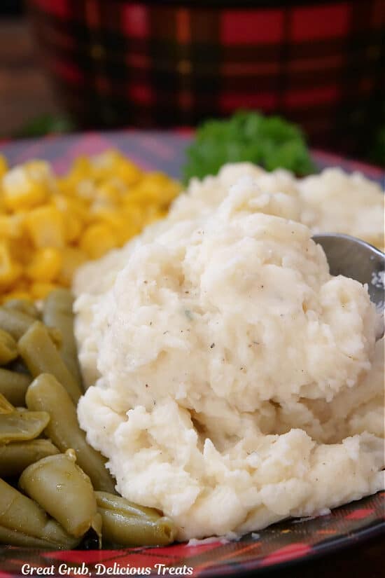 A red and black plate with mashed potatoes, corn and green beans on it.