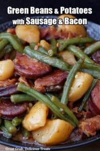 A black bowl with a serving of green beans, potatoes, sausage and bacon.