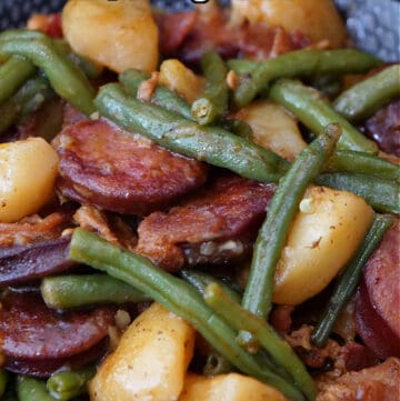 A black bowl with a serving of green beans, potatoes, sausage and bacon.
