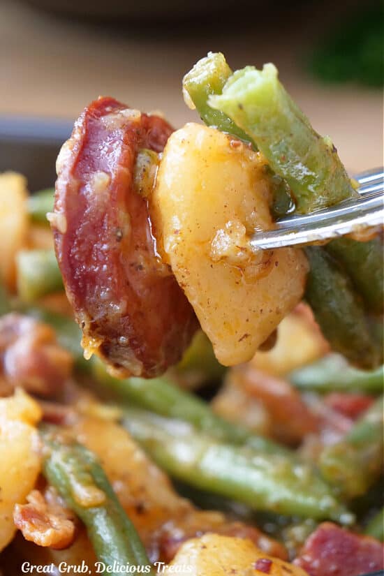 A fork with a bite of sausage, green beans and potato.