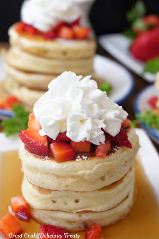 A close up of a stack of three mini pancakes on a white plate, topped with whipped cream and strawberries.