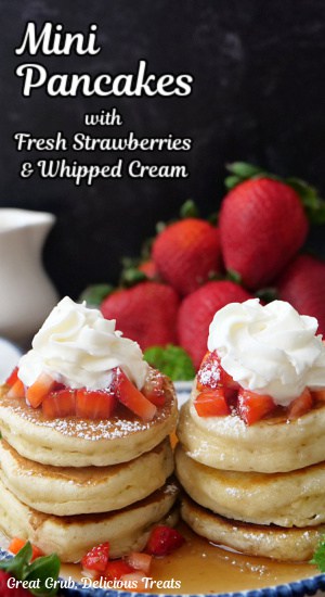 A plate with 6 mini pancakes on it that are topped with strawberries and whipped cream.