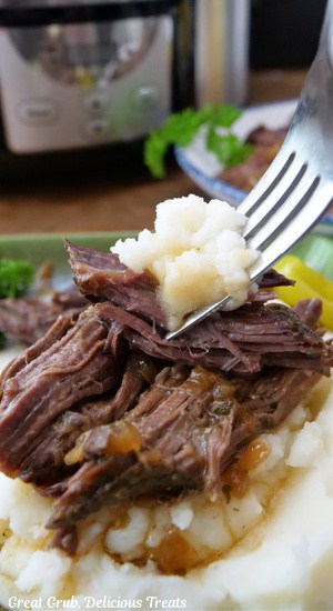 A fork with a bite of beef roast and mashed potatoes on it.