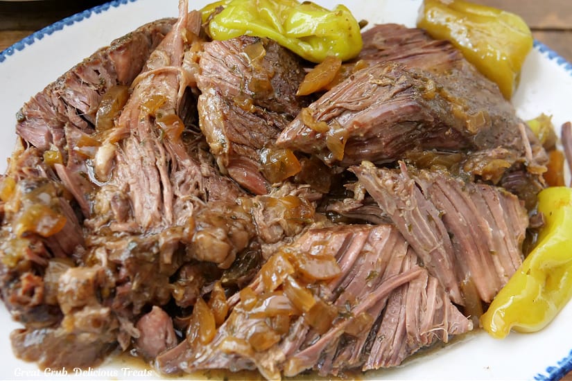 A horizontal photo of a white plate with blue trim with a slow cooked pot roast on it.