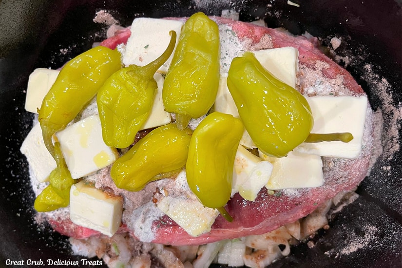 Onion, roast, pepperoncini, butter, au jus mix, ranch dressing mix all in the slow cooker before being cooked.