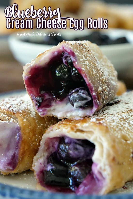 Three blueberry egg rolls on a white plate with blue trim showing the filling inside.