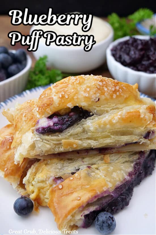 A white plate with three slices of flaky blueberry puff pastry on it.