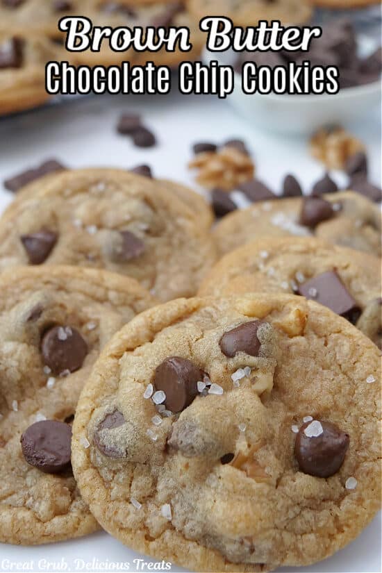 A white surface with chocolate chip cookies on it with more in the background.