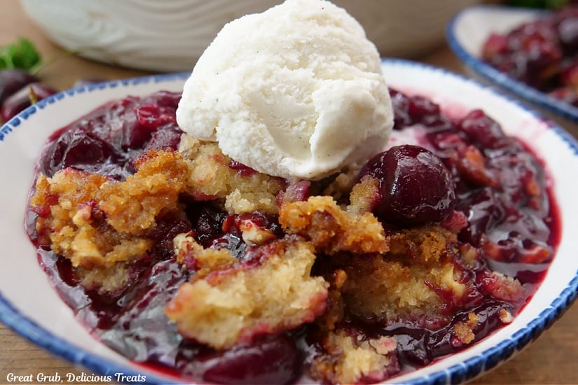 A horizontal photo of a serving of cherry cobbler with vanilla ice cream on top.
