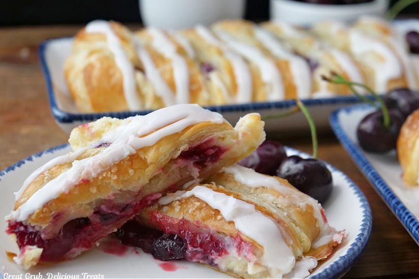 A horizontal photo of puff pastries filled with cherries and cream cheese on white plates with blue trim.