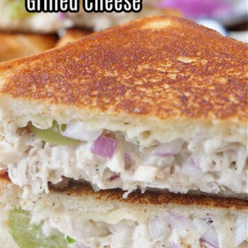 A chicken salad grilled cheese sandwich on a white plate cut in half and one half placed on top of the other half.