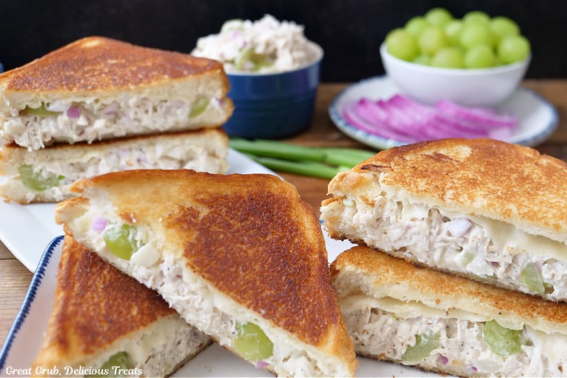 Two white plates with three grilled cheese chicken salad sandwiches cut in half placed on them.