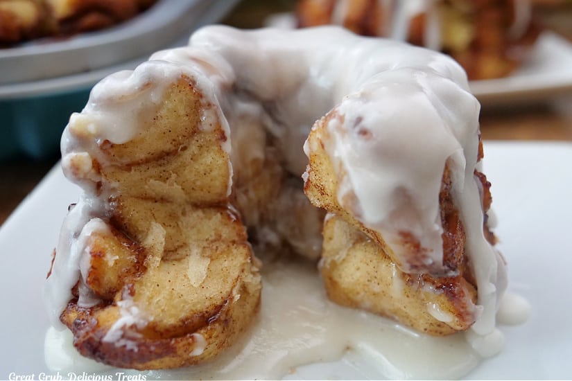 A horizontal photo of a white plate with a mini monkey bread on it that has a few pieces pulled off, and is covered with white icing.