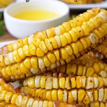 A white plate with a stack of corn ribs on it with a small white bowl filled with melted butter in the background.