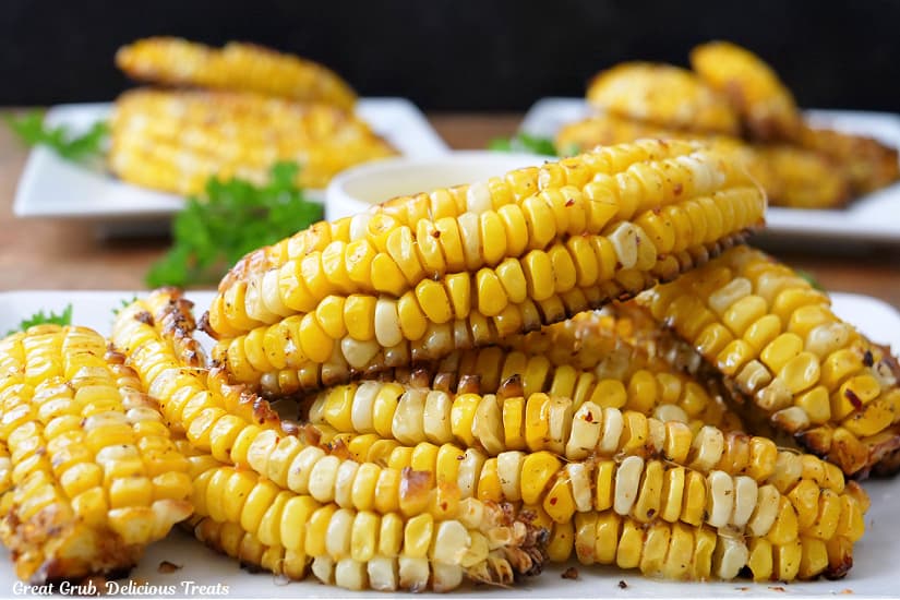 A horizontal photo of three white plates with corn ribs on all of them.