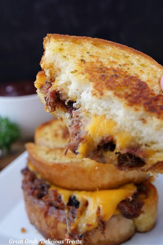 A close up of a BBQ brisket grilled cheese with a few bites taken out of it held up to the camera lens to show the melty cheese and chopped brisket.